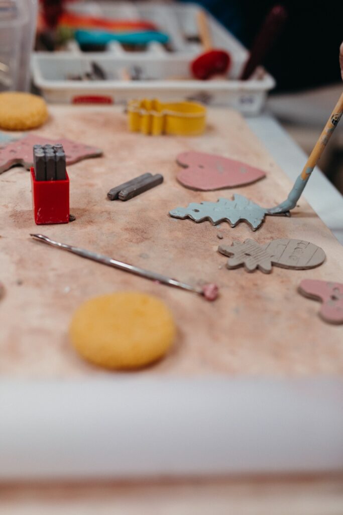 Variously shaped ornaments are spread across a table top, a paintbrush covered with light blue paint covers one of the ornaments