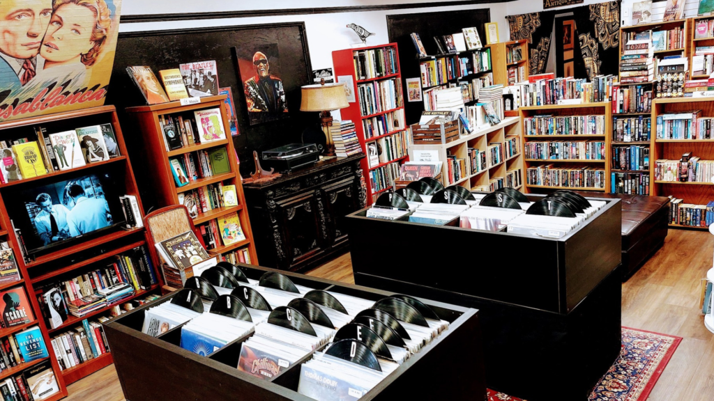 The interior of Groove Cat Books. The back wall is lined with full bookshelves, in the centre of the room are two display tables full of vinyl records.