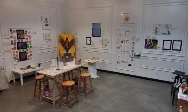 Art covers the white walls of Arrieta Art Studio. A table with four stools sits on the left side of the room covered in art supplies.